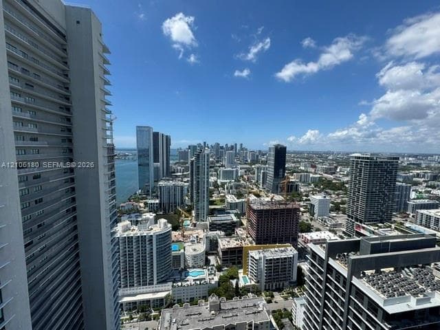 High-rise balcony featuring a metal railing, glass partition, and an expansive cityscape and water horizon