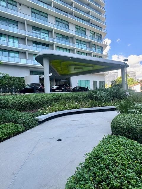Concrete motor court featuring a sculpted porte-cochère with recessed lighting, integrated landscaping, and low-profile stone curbing