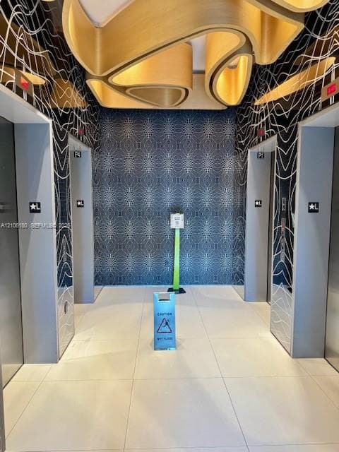 Elevator lobby featuring custom sculptural wood-finish ceiling elements, geometric wall detailing, large-format tile flooring, and metallic elevator doors