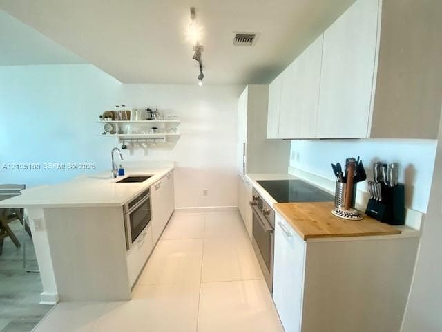 Kitchen featuring white flat-panel cabinetry, quartz countertops, a stainless steel under-mount sink with gooseneck faucet, built-in cooktop, and large-format tile flooring
