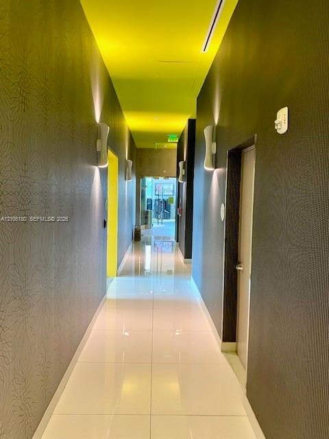 Hallway featuring polished large-format tile flooring, textured wall coverings, and integrated wall-mounted sconce lighting