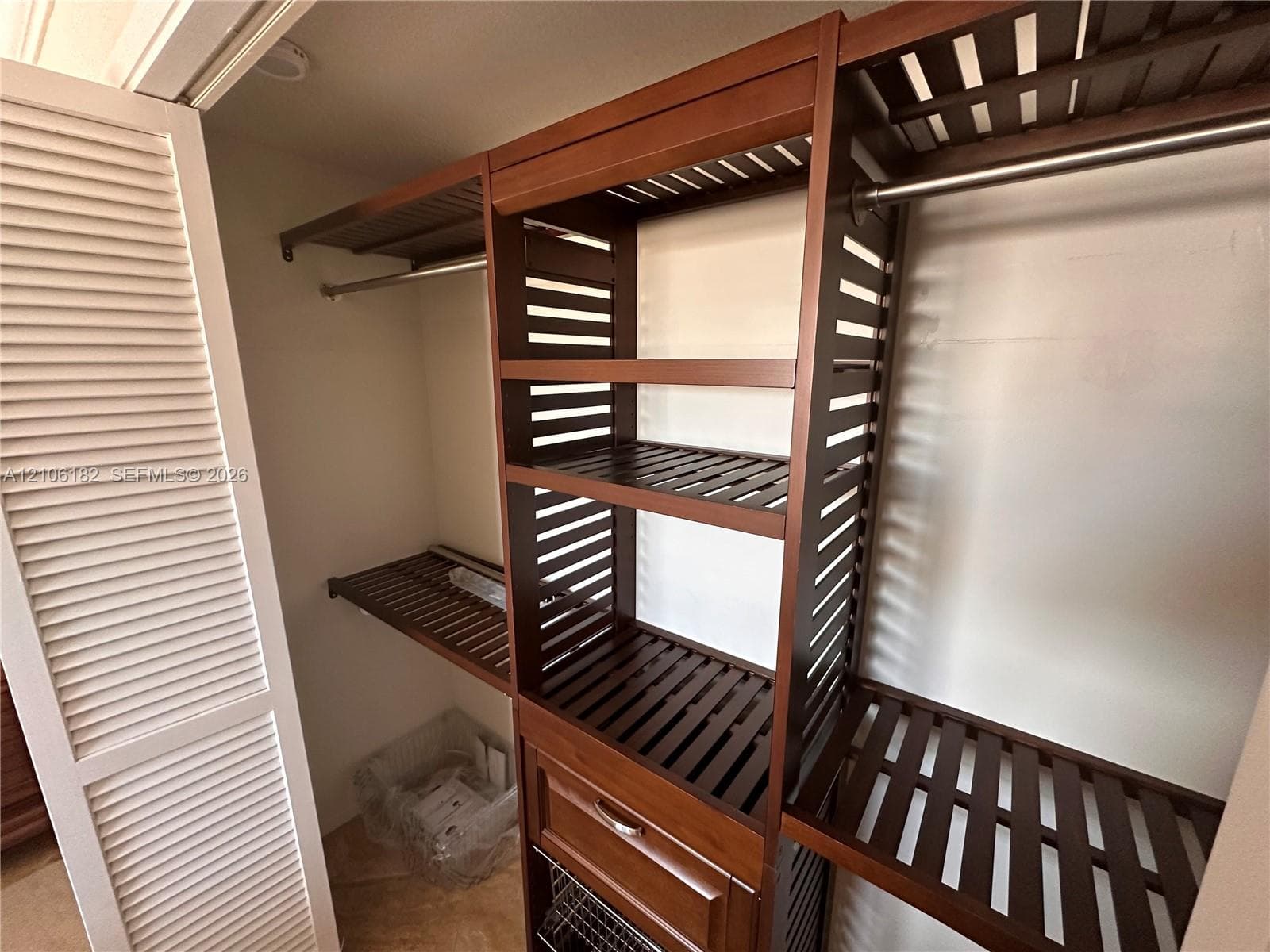 Custom wood-finish closet organizer featuring slatted shelving, a built-in drawer, metallic hanging rods, and louvered folding doors