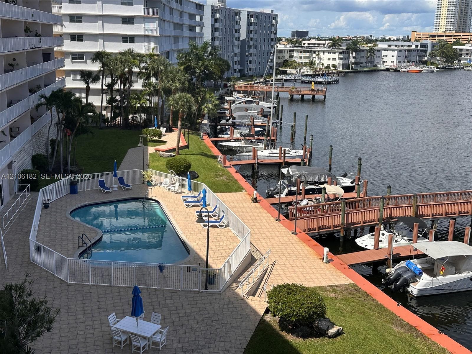 Waterfront swimming pool area featuring paved decking, fenced enclosure, manicured lawn, and attached boat slips