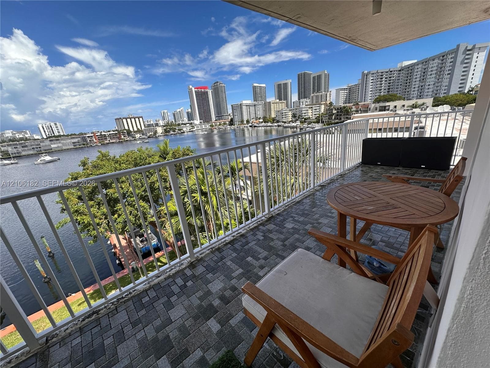 Covered balcony featuring stone-paver flooring and white metal railing with panoramic water and city skyline backdrop