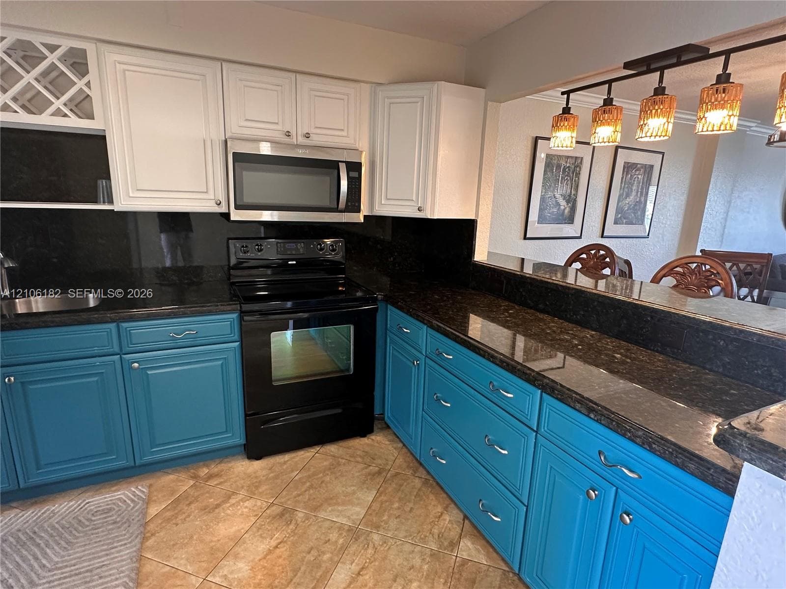 Kitchen featuring dual-toned cabinetry, dark stone-finish countertops, stainless steel appliances, built-in wine storage, and a tiered breakfast bar with multi-pendant overhead lighting