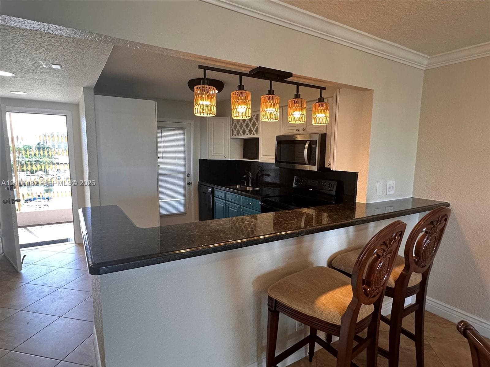 Kitchen featuring dark stone countertops, a raised breakfast bar, built-in wine rack, and a five-light pendant fixture