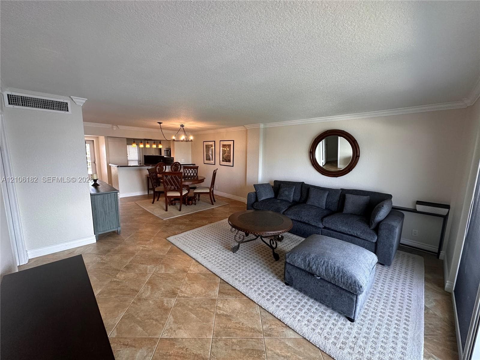 Open-concept interior featuring large-format diagonal floor tiling, crown molding, and a multi-pendant light fixture over the dining area