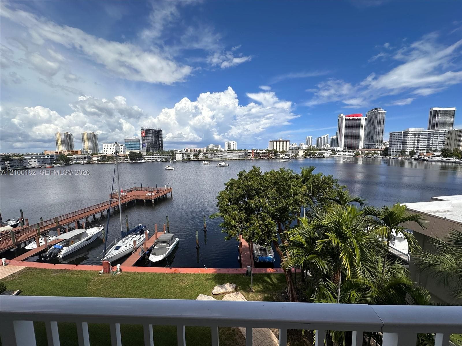 Waterfront setting featuring a private dock, boat slips, mature landscaping, and an expansive cityscape backdrop