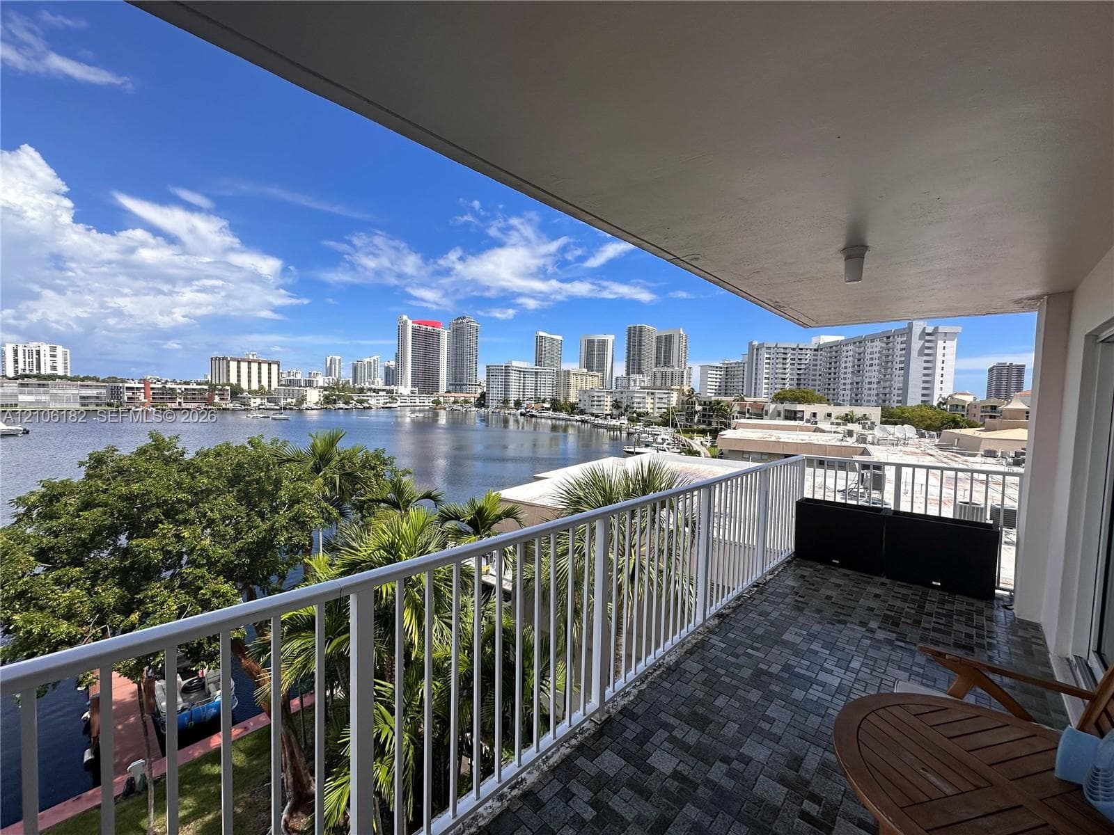 Covered balcony featuring white vertical railing, textured flooring, and water and skyline scenery