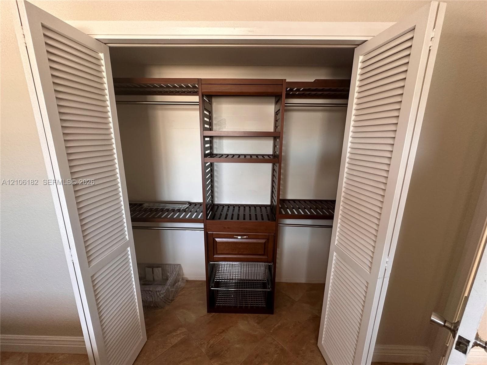 Closet featuring white louvered bifold doors, built-in wooden shelving, integrated storage drawers, pull-out wire organizing baskets, and tile flooring