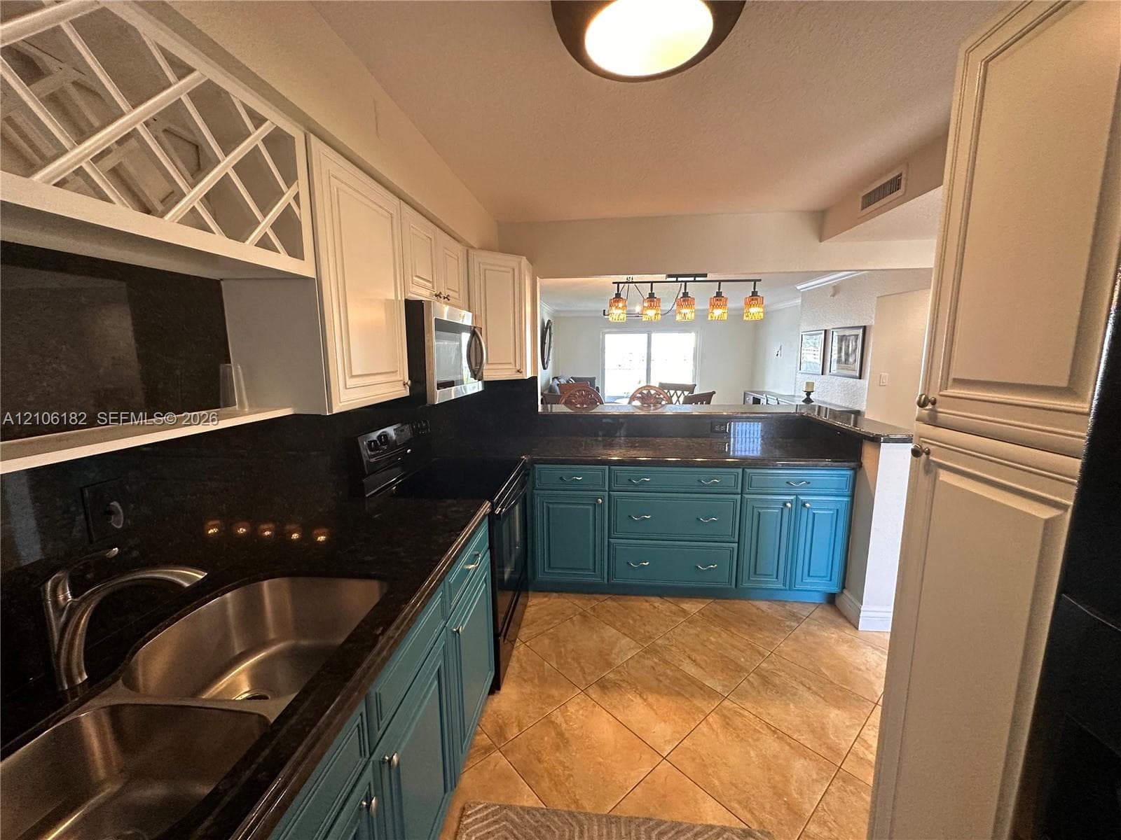 Kitchen featuring two-tone cabinetry, dark stone countertops, diamond-pattern upper cabinet inserts, a dual-basin stainless steel sink, and diagonal-set tile flooring