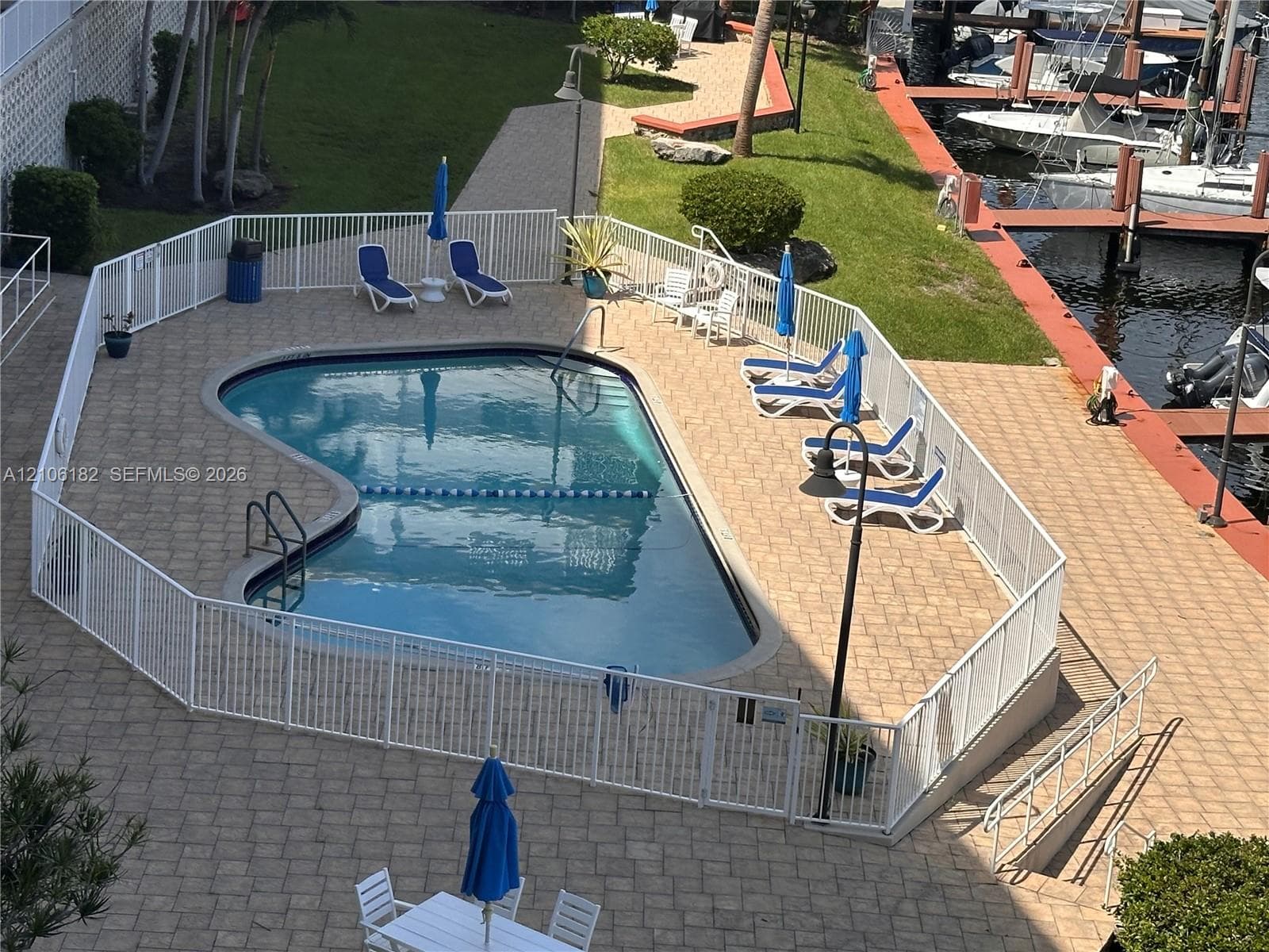 Inground swimming pool with paver decking and white perimeter fencing, situated on a waterfront lot with dock access