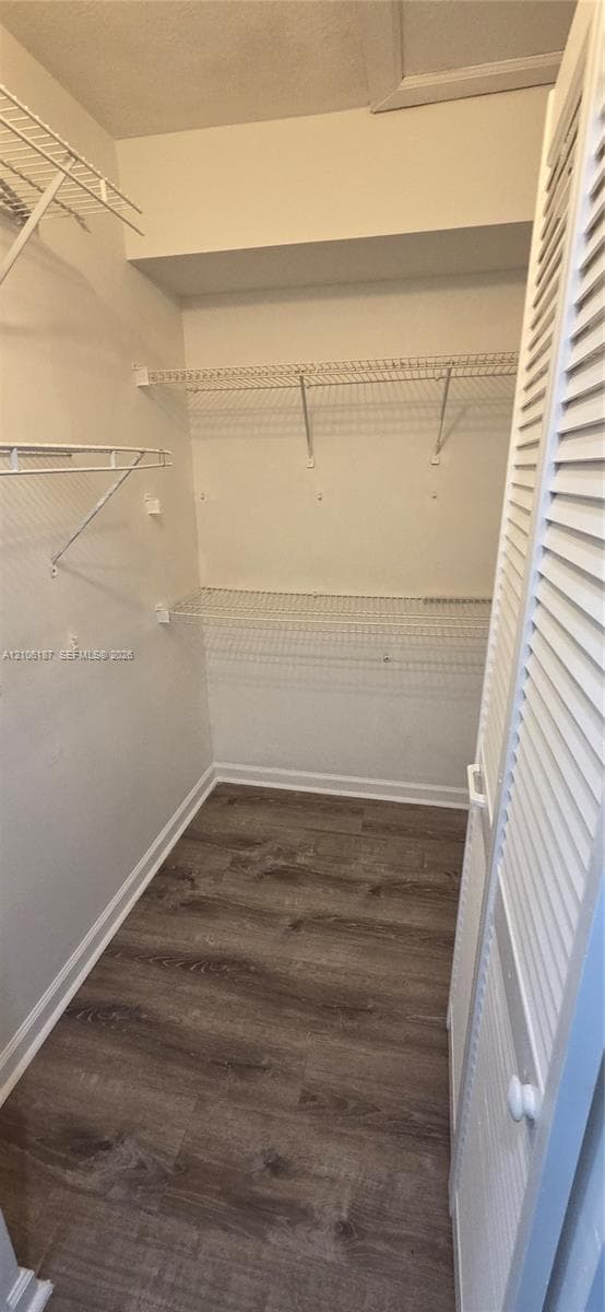 Storage area featuring wood-finish flooring, white louvered doors, and built-in wire shelving