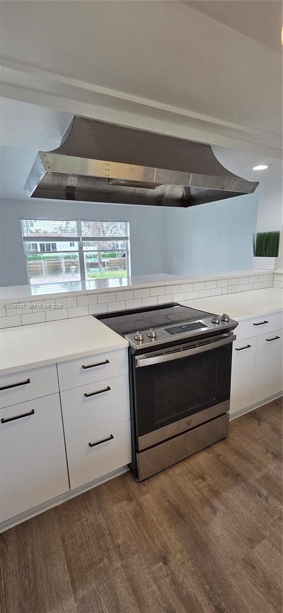 Stainless steel freestanding range, custom metal range hood, white cabinetry with matte black hardware, white solid-surface countertops, and subway tile backsplash
