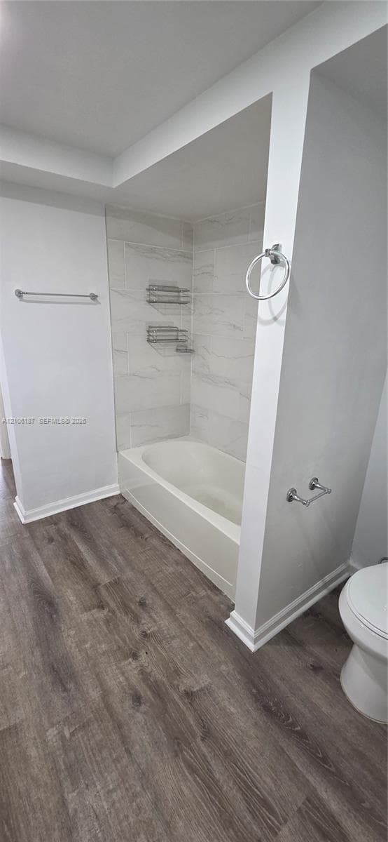 Full bathroom featuring a tub-shower combination with floor-to-ceiling stone-style wall tile, integrated wire shelving, wood-finish flooring, and wall-mounted metal hardware
