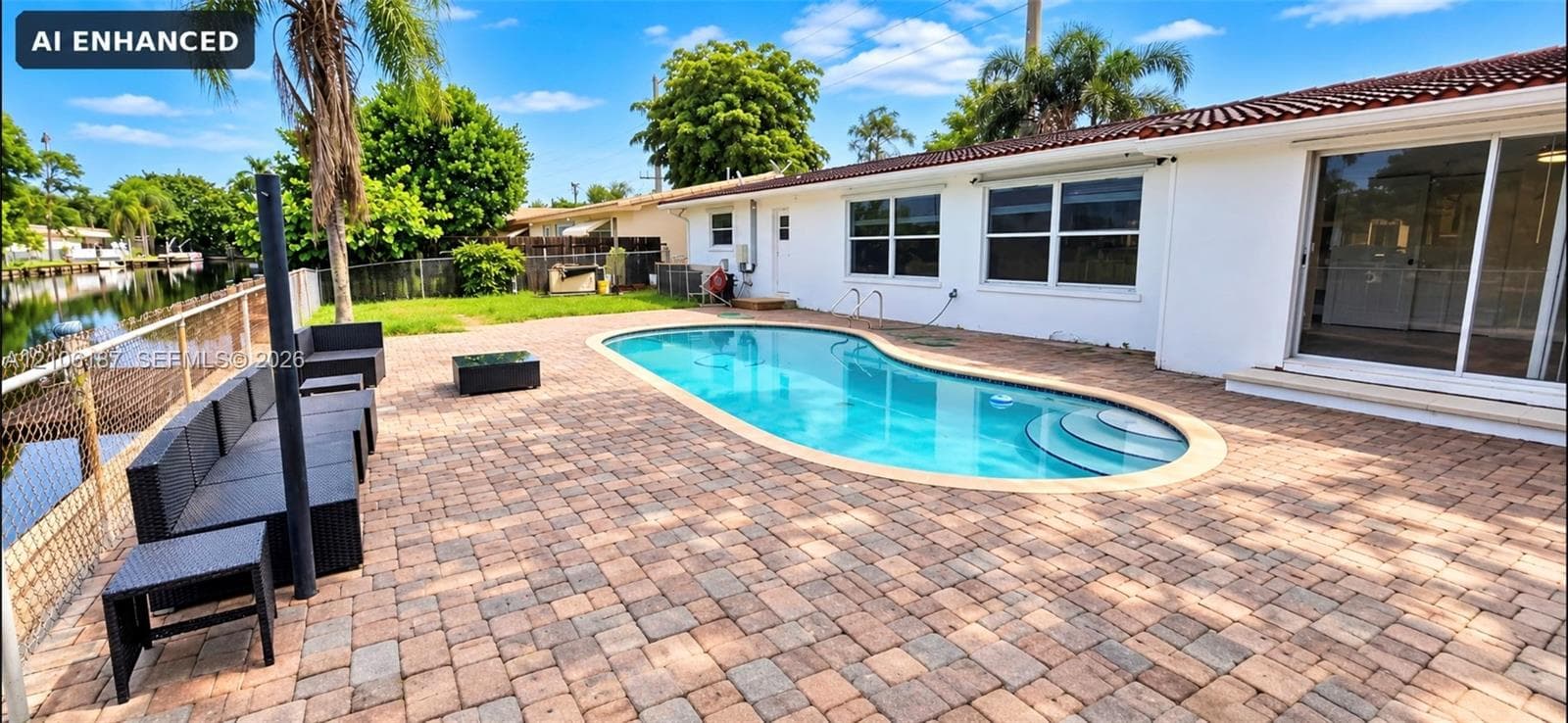 Rear exterior featuring a paver patio, in-ground swimming pool with integrated steps, waterfront bulkhead, and sliding glass doors