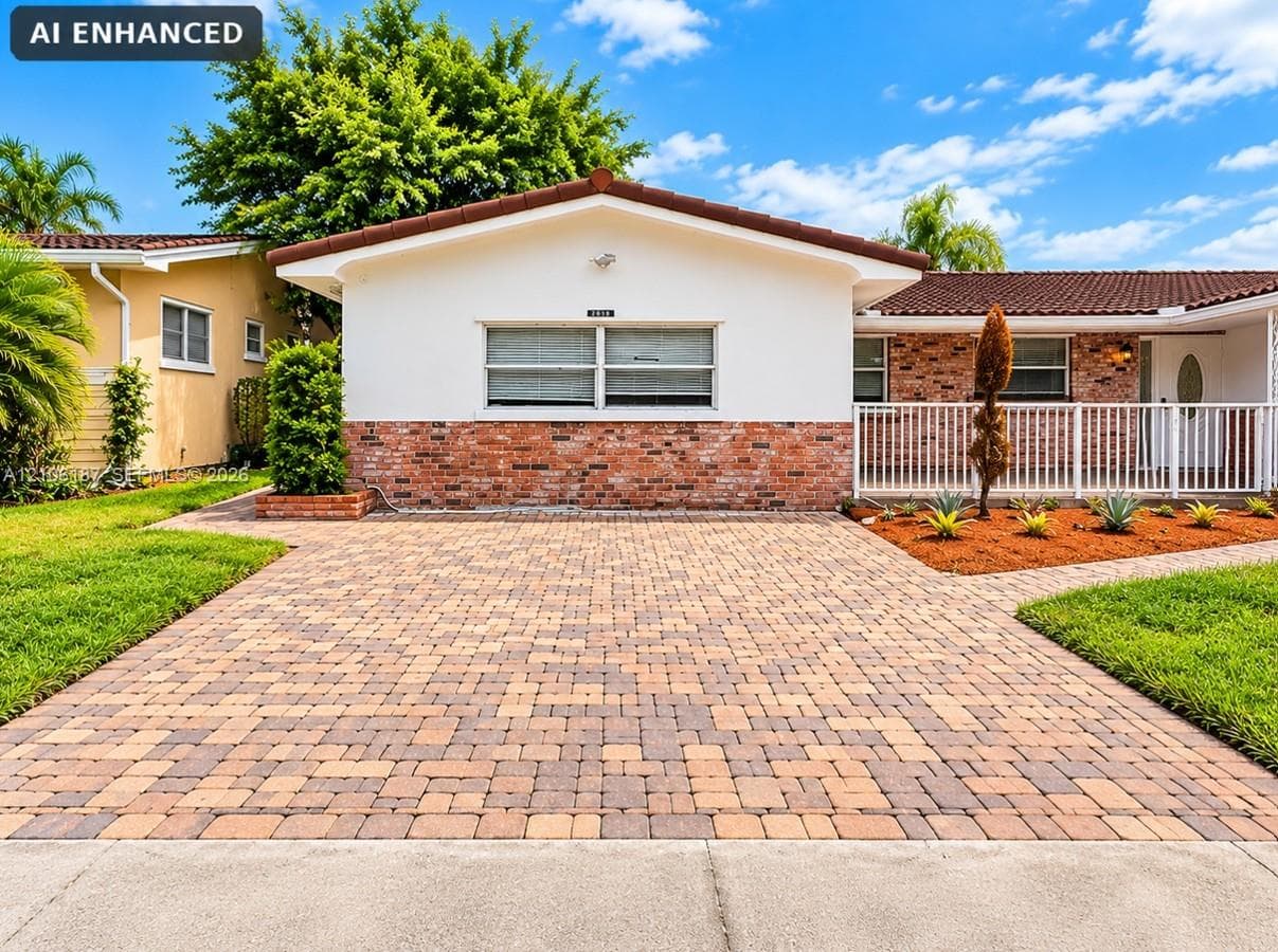 Single-story exterior featuring a brick and stucco facade, concrete paver driveway, tile roof, and white metal front porch railing