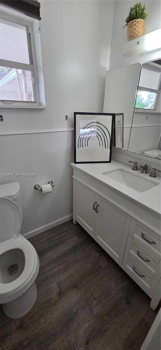 White vanity with stone-surface countertop, rectangular undermount sink, wood-finish flooring, and wall-mounted wainscoting