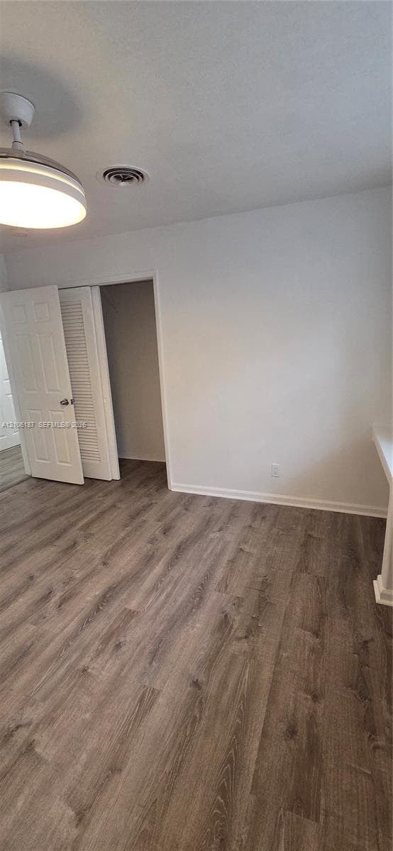 Interior space featuring wood-finish flooring, a neutral color palette, built-in closet with louvered doors, and a central ceiling-mounted light fixture