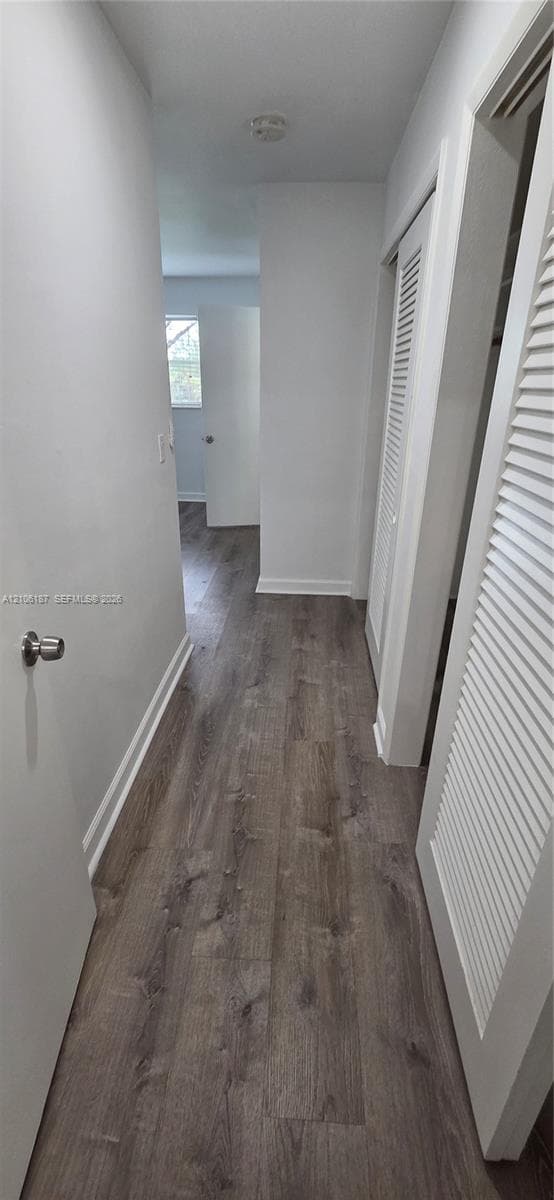 Hallway featuring wood-finish flooring, white walls, and dual louvered closet doors
