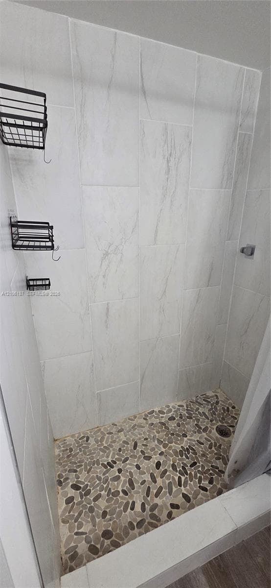 Walk-in shower featuring floor-to-ceiling large-format tile walls and a textured natural stone pebble shower floor