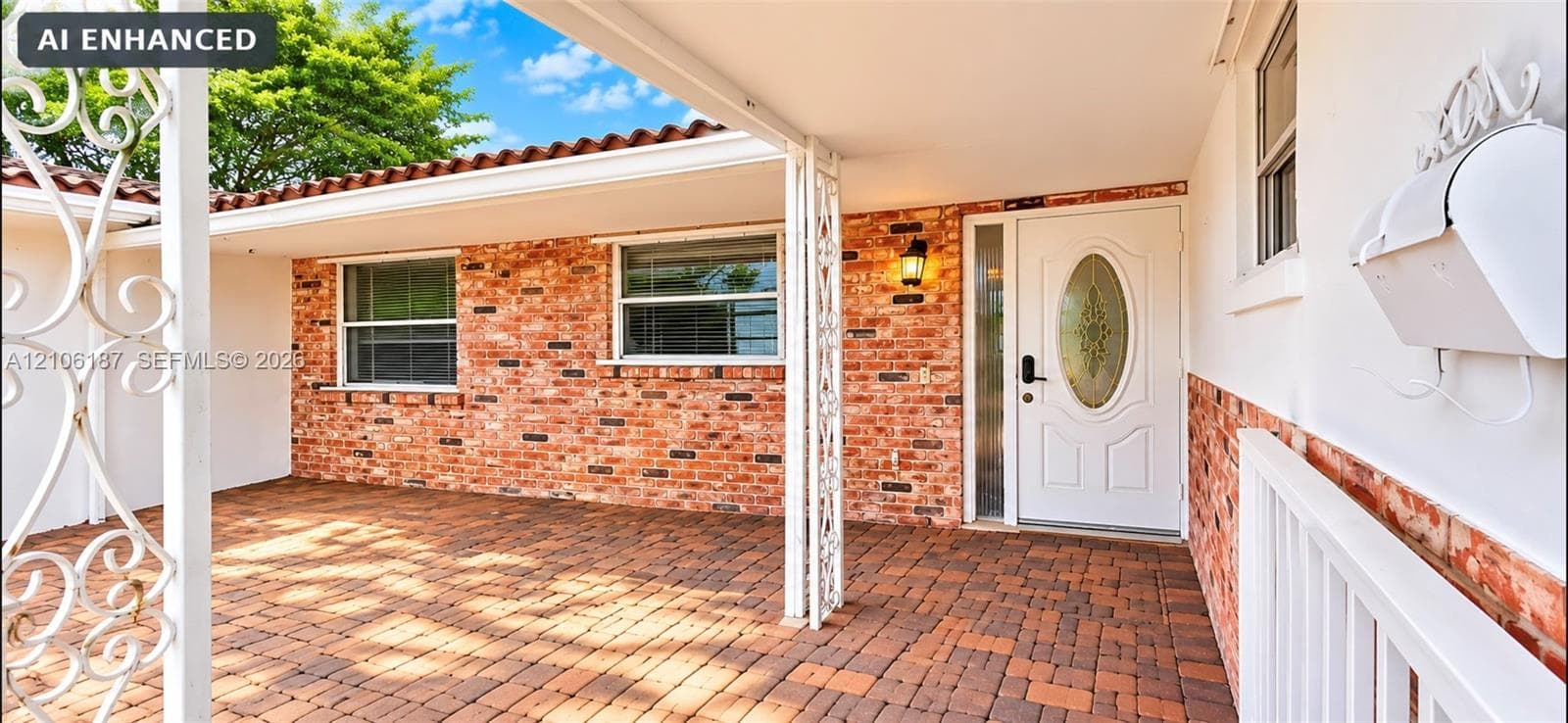 Covered front entry featuring red brick exterior siding, terracotta-style roof tiles, decorative metal porch supports, and a paved brick porch