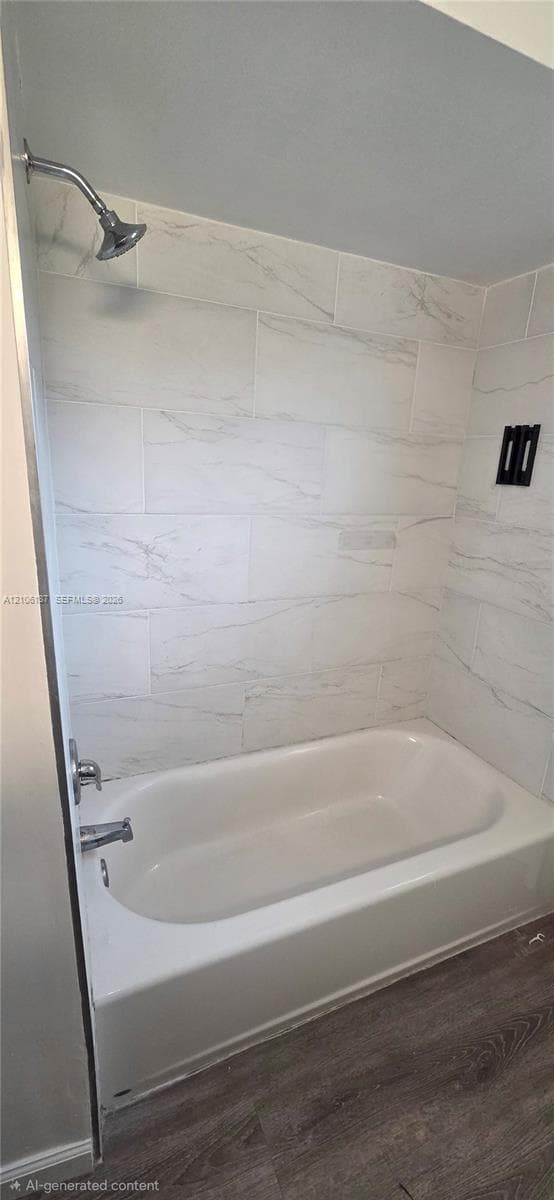 Bathtub and shower combination featuring large-format stone-patterned wall tile, chrome hardware, and wood-finish flooring