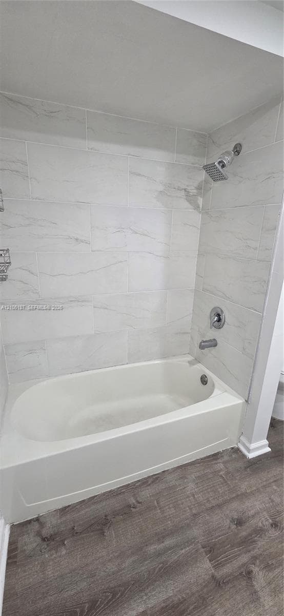 Bathtub and shower combination featuring wall-to-ceiling large-format stone-patterned tile, chrome fixtures, and wood-finish flooring