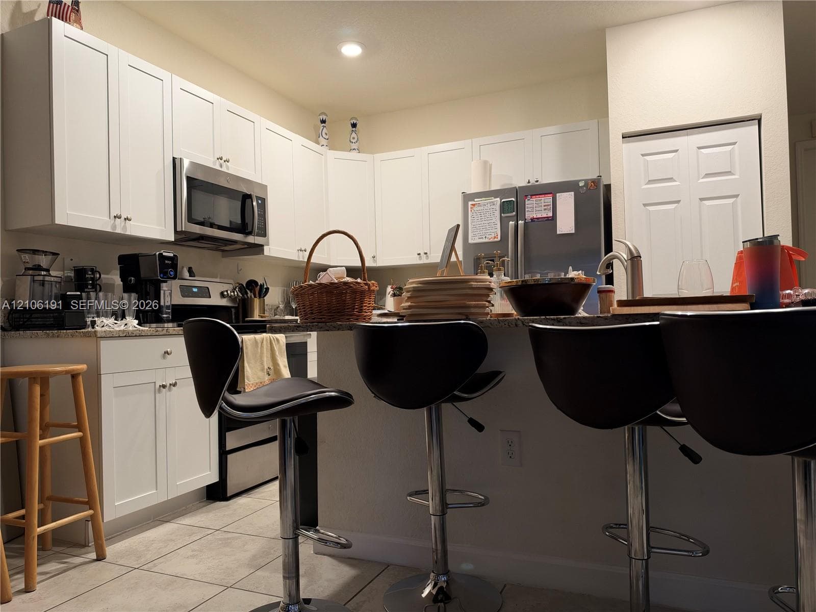 Kitchen featuring white shaker-style cabinetry, stone countertops, stainless steel appliances, and a breakfast bar with a chrome faucet