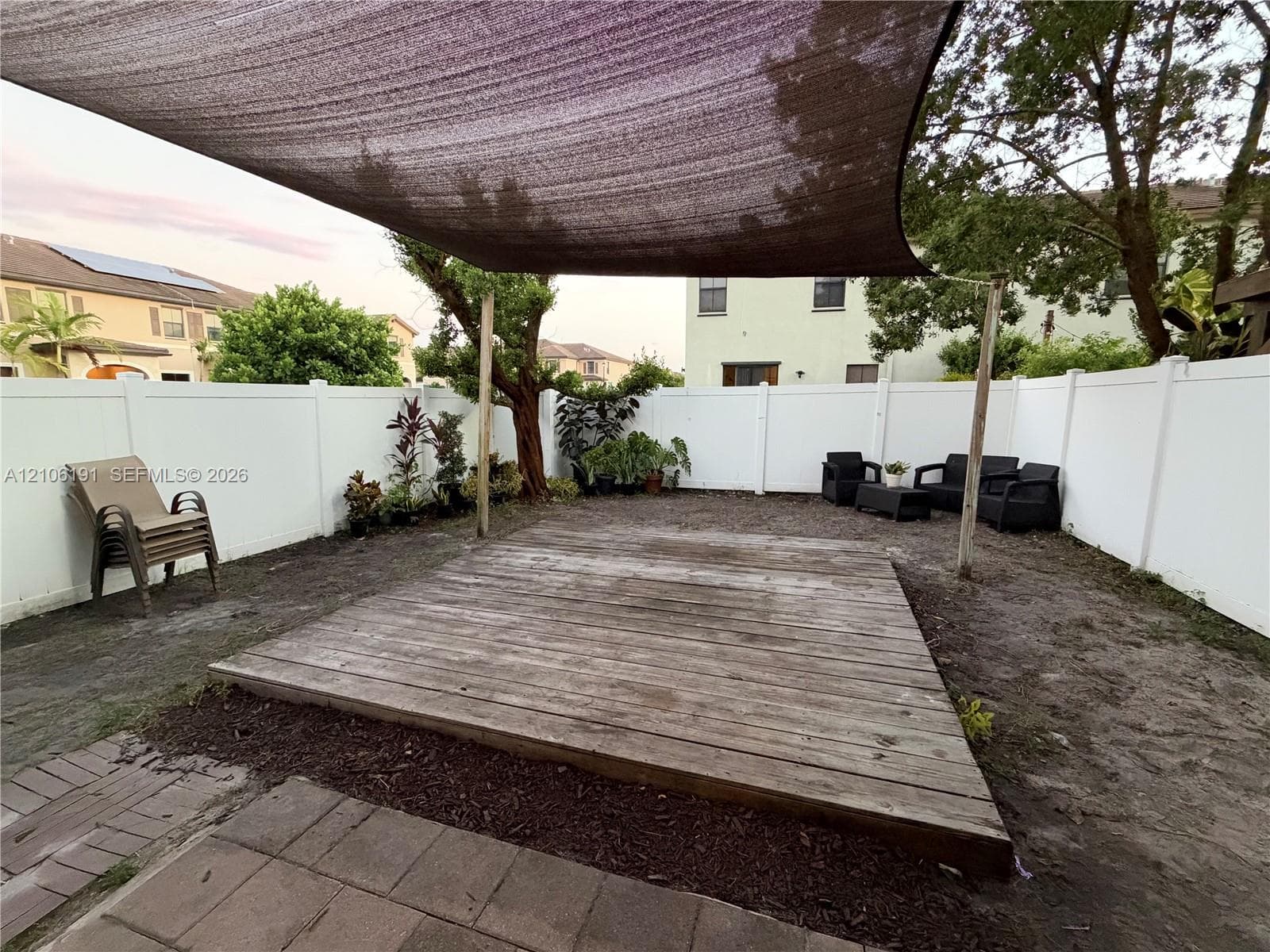 Backyard featuring a wood deck, a tensioned shade canopy, a white vinyl privacy fence, and brick paver accents