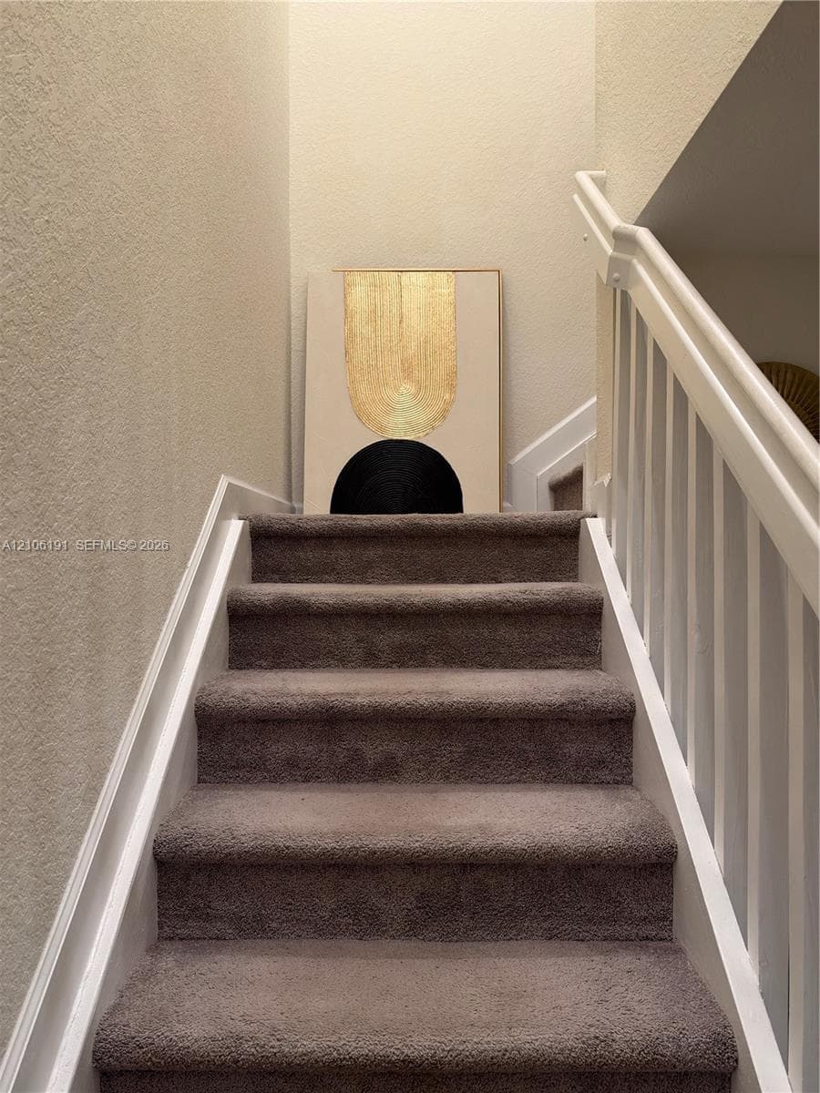 Staircase featuring wall-to-wall carpeting, white painted wooden balusters, and a matching handrail