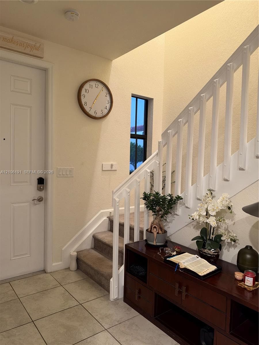 Entryway featuring ceramic tile flooring, a painted white staircase with a vertical balustrade, carpeted stair treads, and a multi-pane window