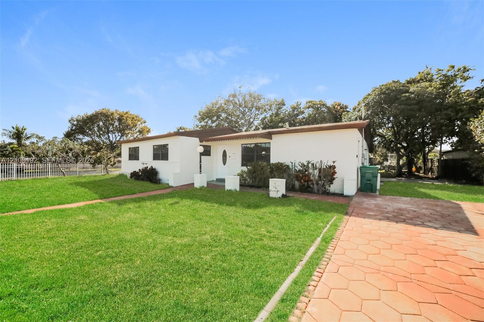 Single-story residence featuring a smooth stucco exterior, low-pitch roofline, expansive manicured lawn, and a hexagonal paver driveway