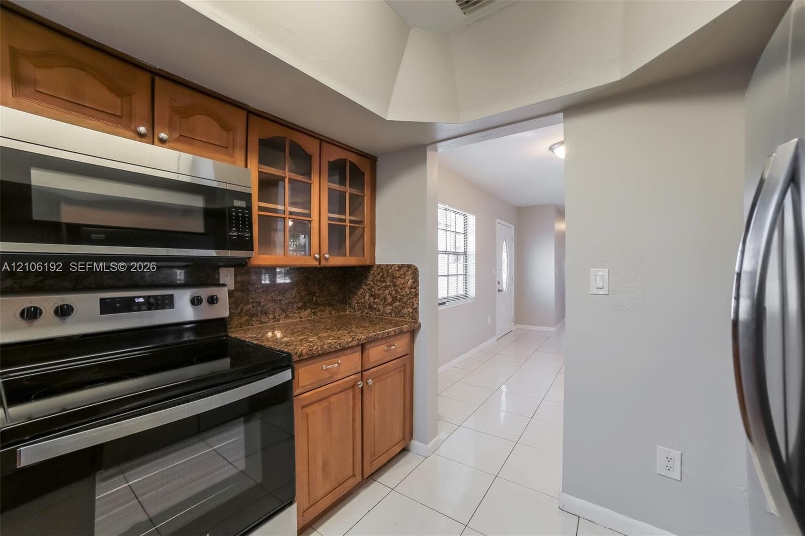 Kitchen featuring natural-finish wood cabinetry with glass-front display panels, speckled stone-finish countertops, stainless steel appliances, and a vaulted ceiling