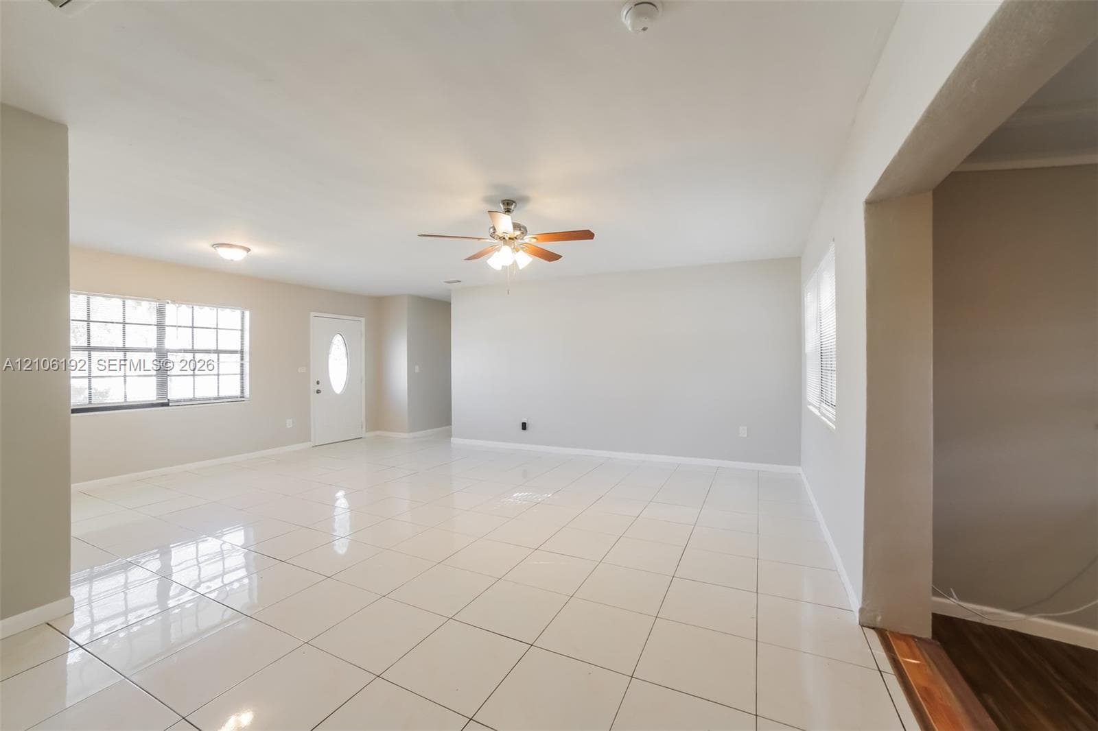 Neutral interior featuring white ceramic tile flooring, a multi-blade ceiling fan with integrated lighting, and white-paneled entry door with an oval glass insert