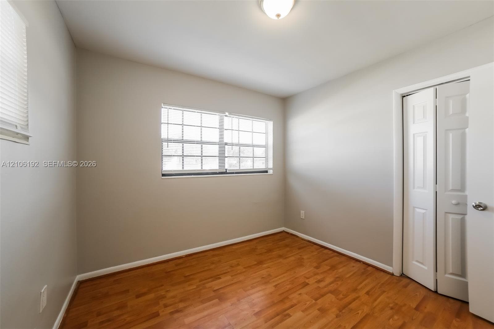 Room featuring wood-finish flooring, neutral wall paint, a multi-pane window, and a closet with paneled bifold doors