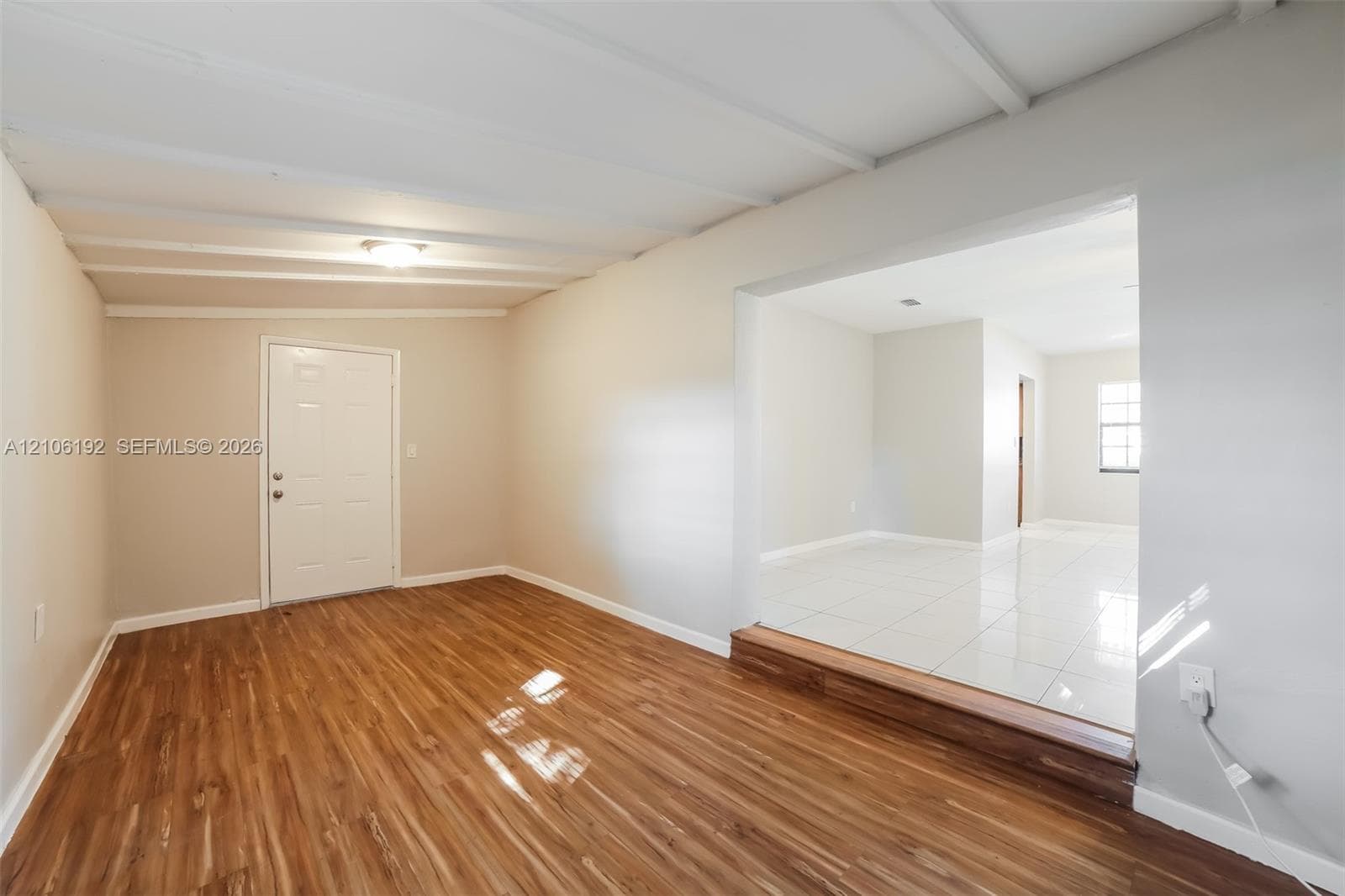 Wood-finish flooring, tray ceiling with exposed structural beams, raised threshold, and large-format tile flooring
