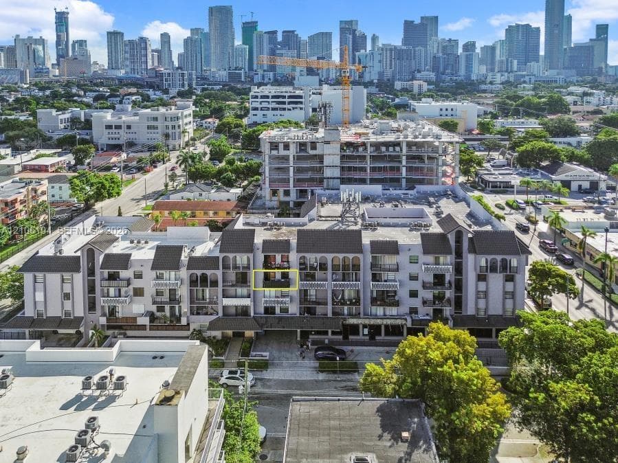 Multi-story residential building featuring arched architectural accents, a private balcony, a flat roofline, and proximity to an urban skyline