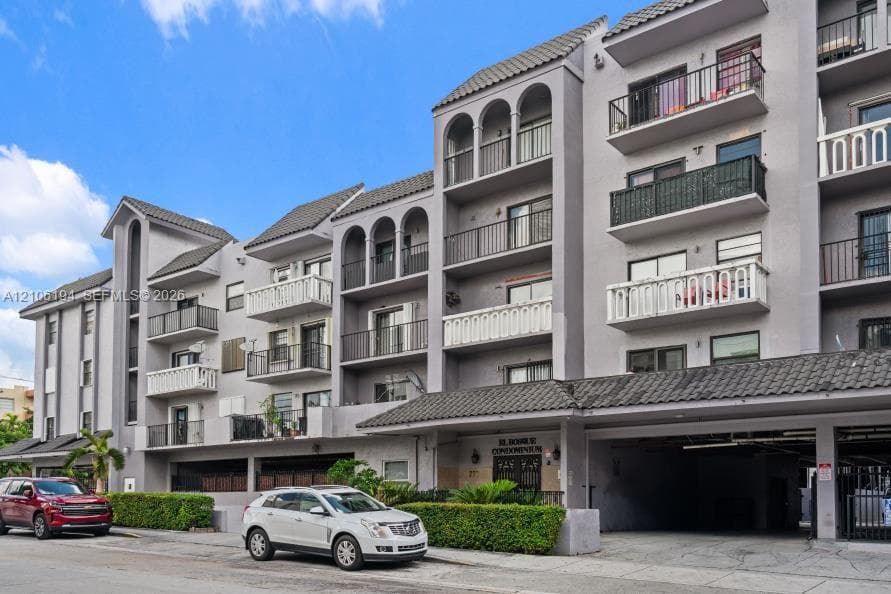 Multi-story condominium exterior featuring arched architectural detailing, private balconies with metal railings, tile roof accents, and integrated covered parking