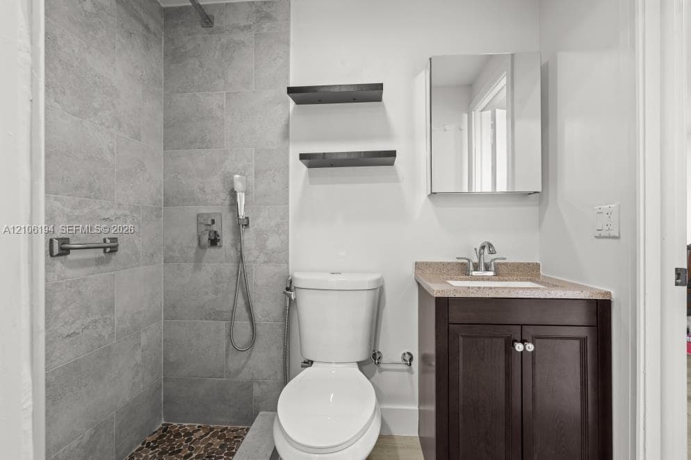 Bathroom featuring a walk-in shower with stone-style tile surround and pebble tile flooring, dark-finish cabinetry with a speckled countertop, wall-mounted medicine cabinet, and built-in wall shelving