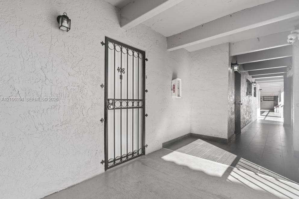 Covered exterior walkway featuring textured stucco walls, concrete flooring, decorative metal security door, and wall-mounted exterior lanterns
