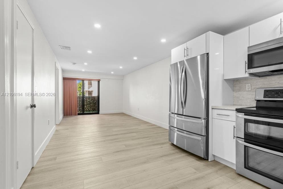 Modern kitchen featuring white flat-panel cabinetry, stainless steel appliances, wood-laminate flooring and recessed ceiling lighting