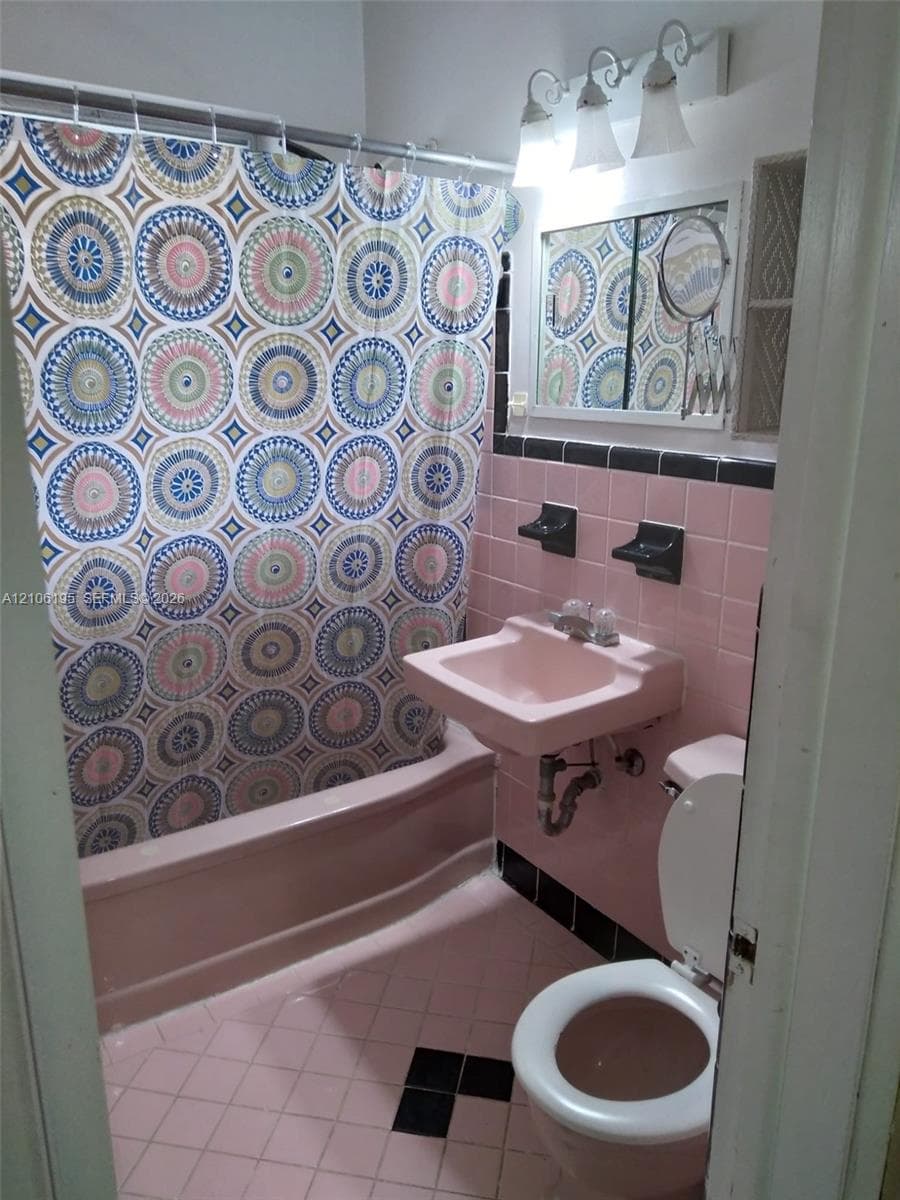 Bathroom featuring pink wall tiling with black accent trim, wall-mounted sink, built-in shelving, and a three-light vanity fixture