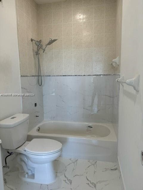 Bathtub featuring stone-pattern wall tile, hand-held shower fixture, and stone-pattern floor tile