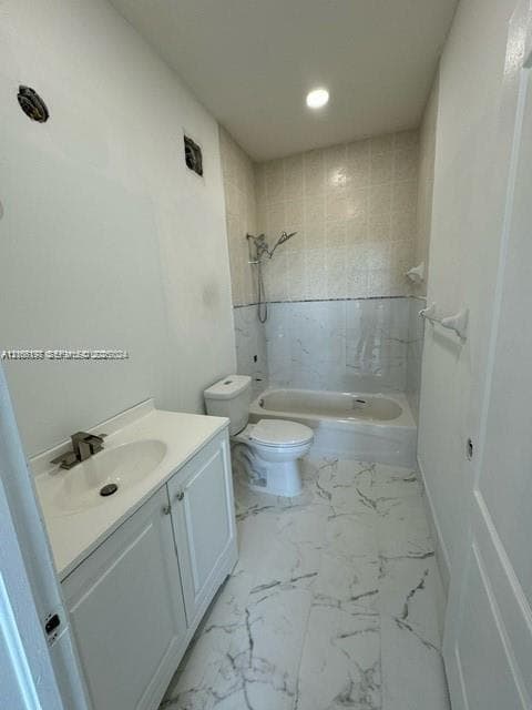 Bathroom featuring a vanity with an integrated sink, polished faucet, white shaker-style cabinetry, and a combination tub and shower with light-toned tiled surrounds and veined stone-patterned floor tile