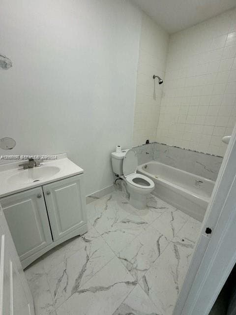 Bathroom featuring large-format white tile flooring with grey veining, a white vanity with an integrated sink, a porcelain toilet, and a bathtub with tile surround