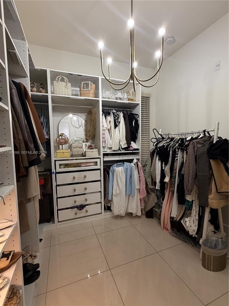 Custom storage system featuring floor-to-ceiling white cabinetry, integrated drawers with gold-tone hardware, polished tile flooring, and a multi-arm metallic chandelier