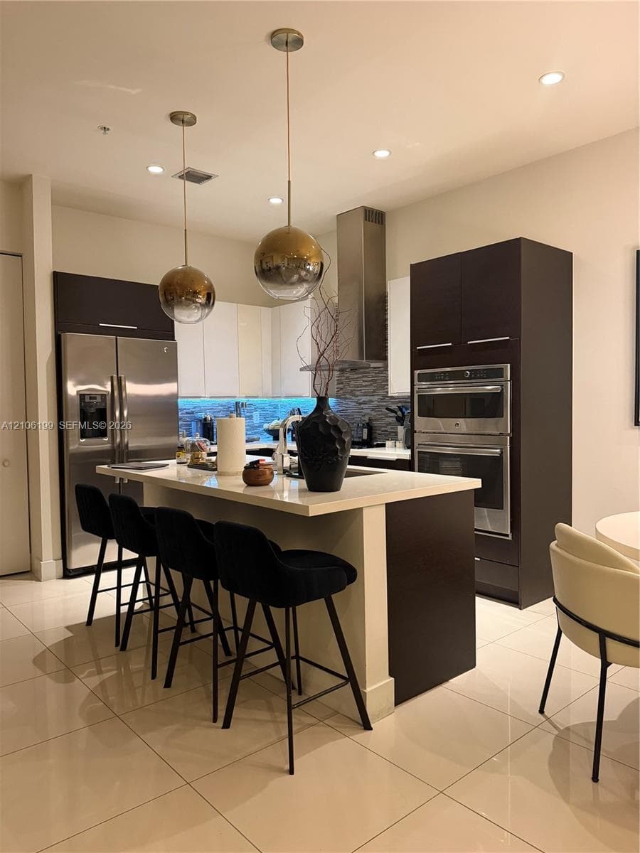 Kitchen featuring custom flat-panel cabinetry, a central island with stone-finish countertops, stainless steel built-in double wall ovens, recessed lighting, and spherical pendant fixtures