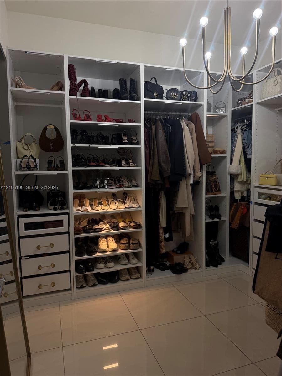 Custom built-in storage system featuring floor-to-ceiling white cabinetry, integrated shelving, pull-out drawers with metallic hardware, and a multi-arm modern light fixture over tile flooring