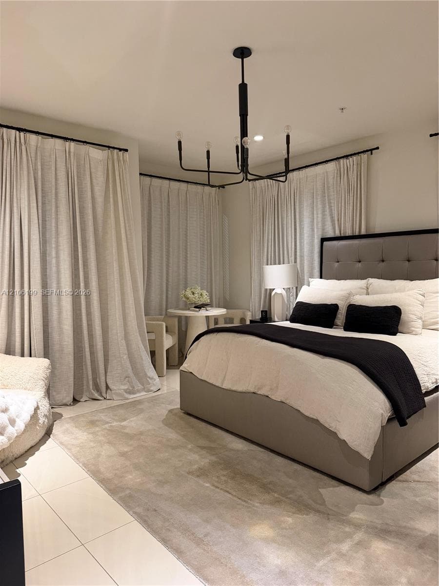 Spacious room featuring light-toned tile flooring, floor-to-ceiling drapery panels on black hardware, and a multi-arm geometric chandelier with a black finish